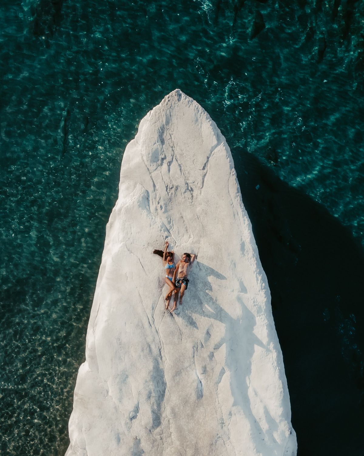 Swimmers resting on a rock in turquoise water